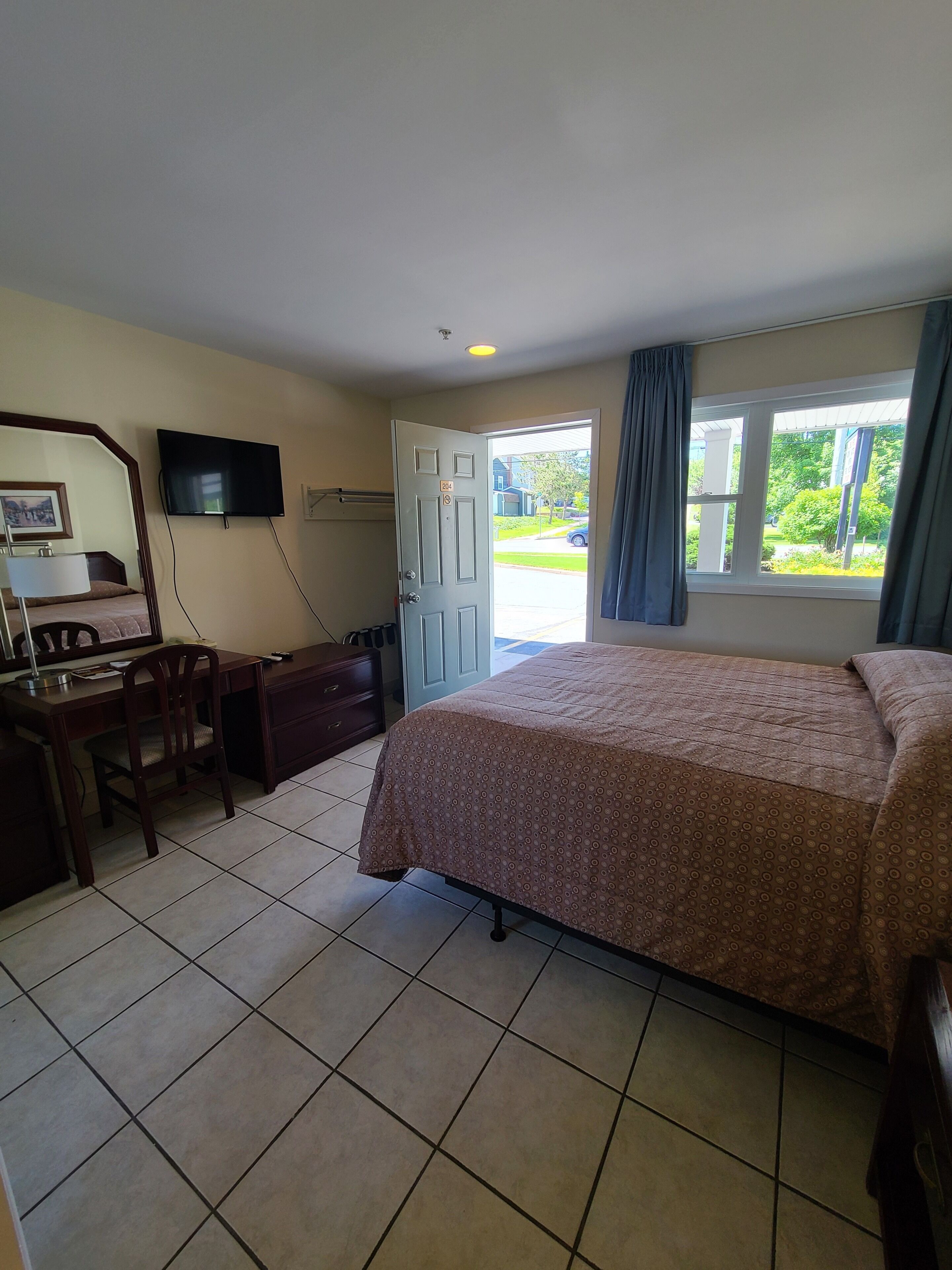 Una habitación de hotel con cama, escritorio, silla, televisor y ventana con cortinas.