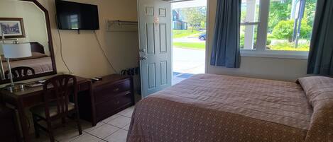 A hotel room with a bed, a desk, a chair, a television, and a window with curtains.