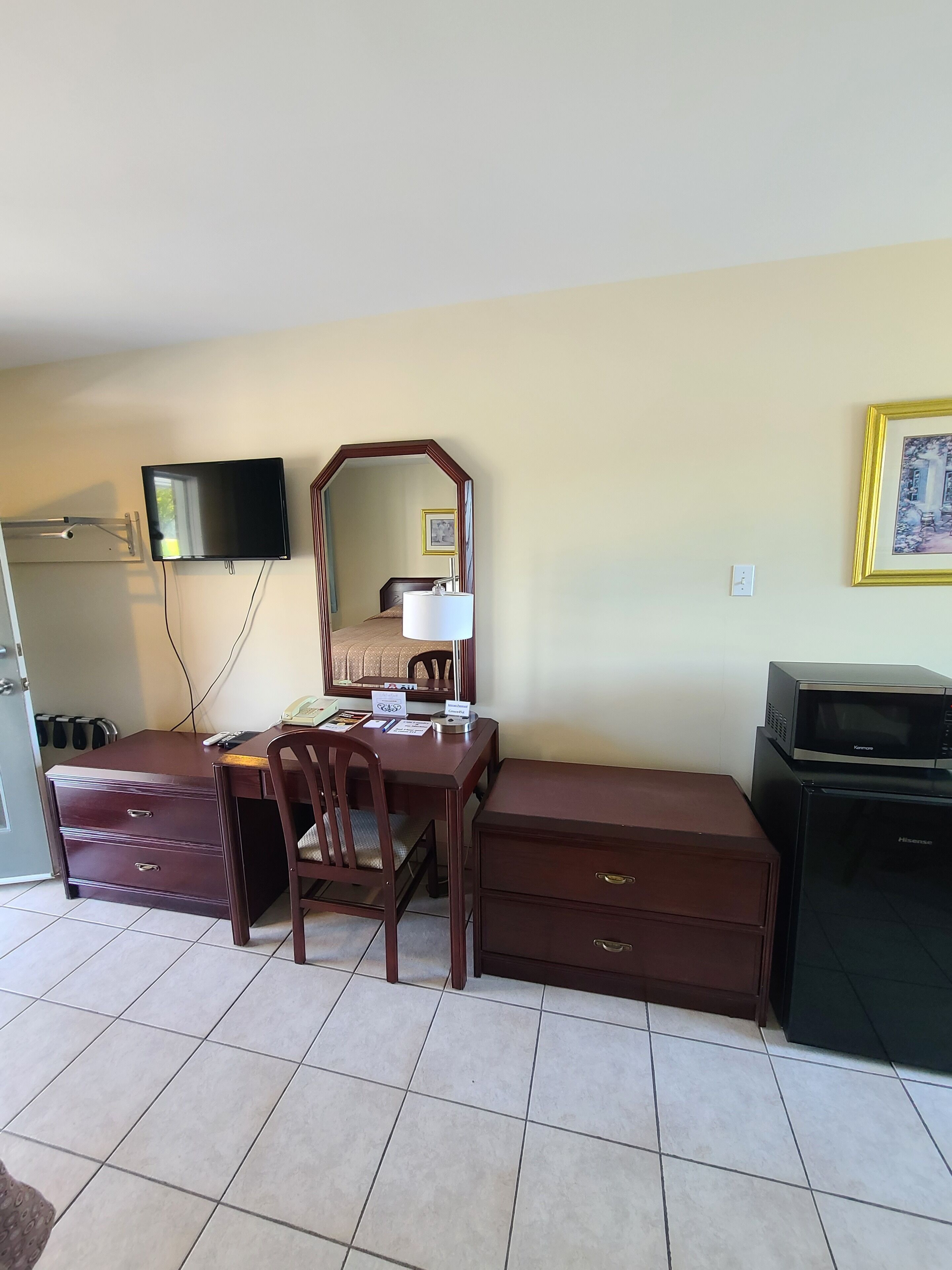 A compact room with a desk, chair, dresser, and a television mounted on the wall.