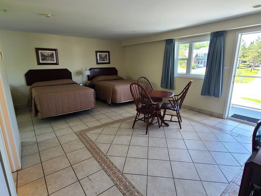A hotel room with two beds, a dining table with chairs, and large windows with curtains.