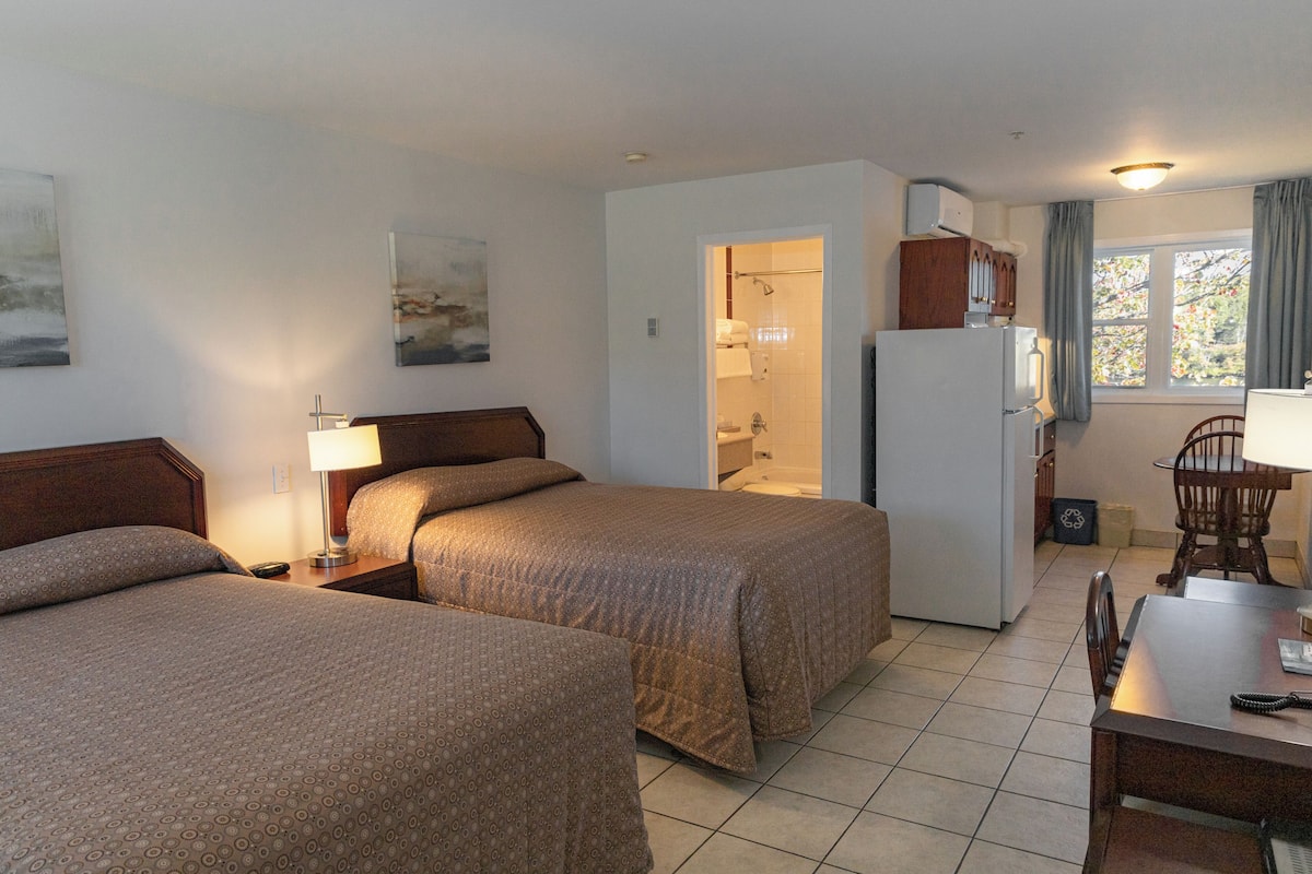 A hotel room with two beds, a small kitchenette, a bathroom, and a dining area.