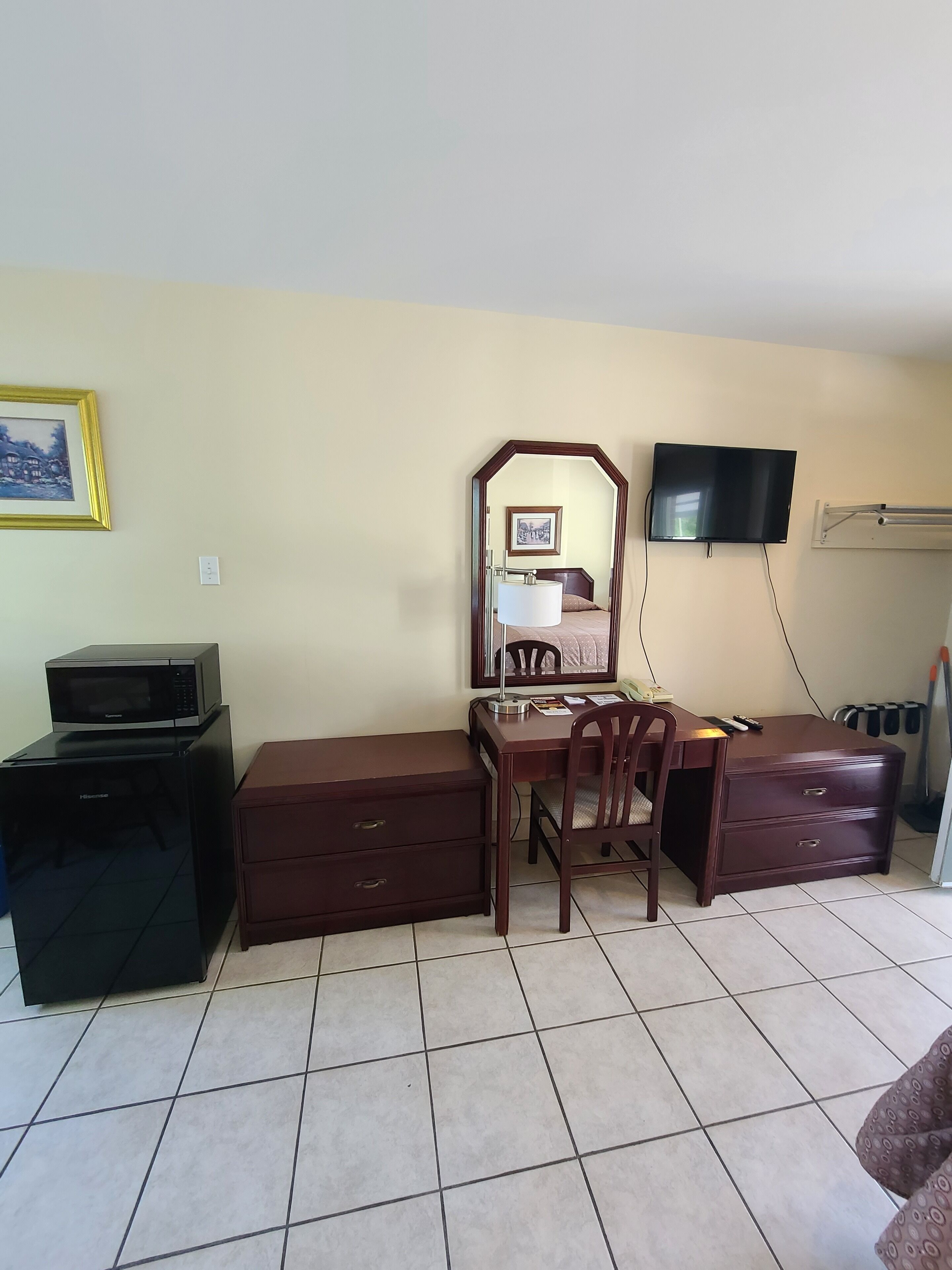 A hotel room with a desk, a chair, a dresser, a television mounted on the wall, and a microwave on the floor.