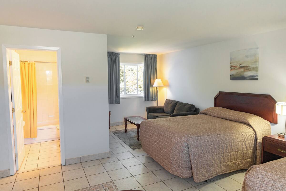 A hotel room with a bed, a desk, a chair, a window with curtains, and a painting on the wall.
