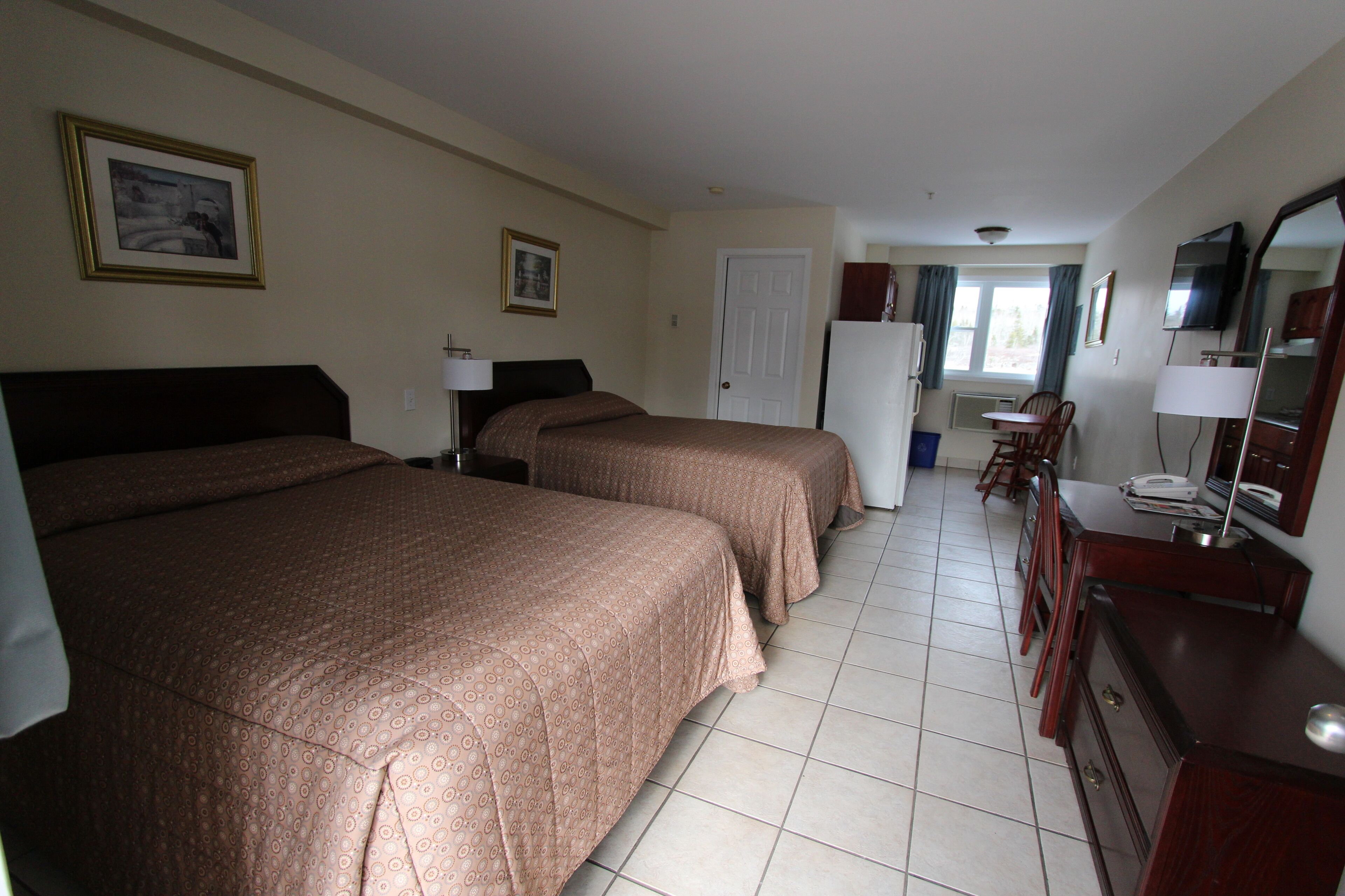 Une chambre d’hôtel avec deux lits, un bureau avec une chaise, une commode, une télévision et une porte donnant sur un balcon.