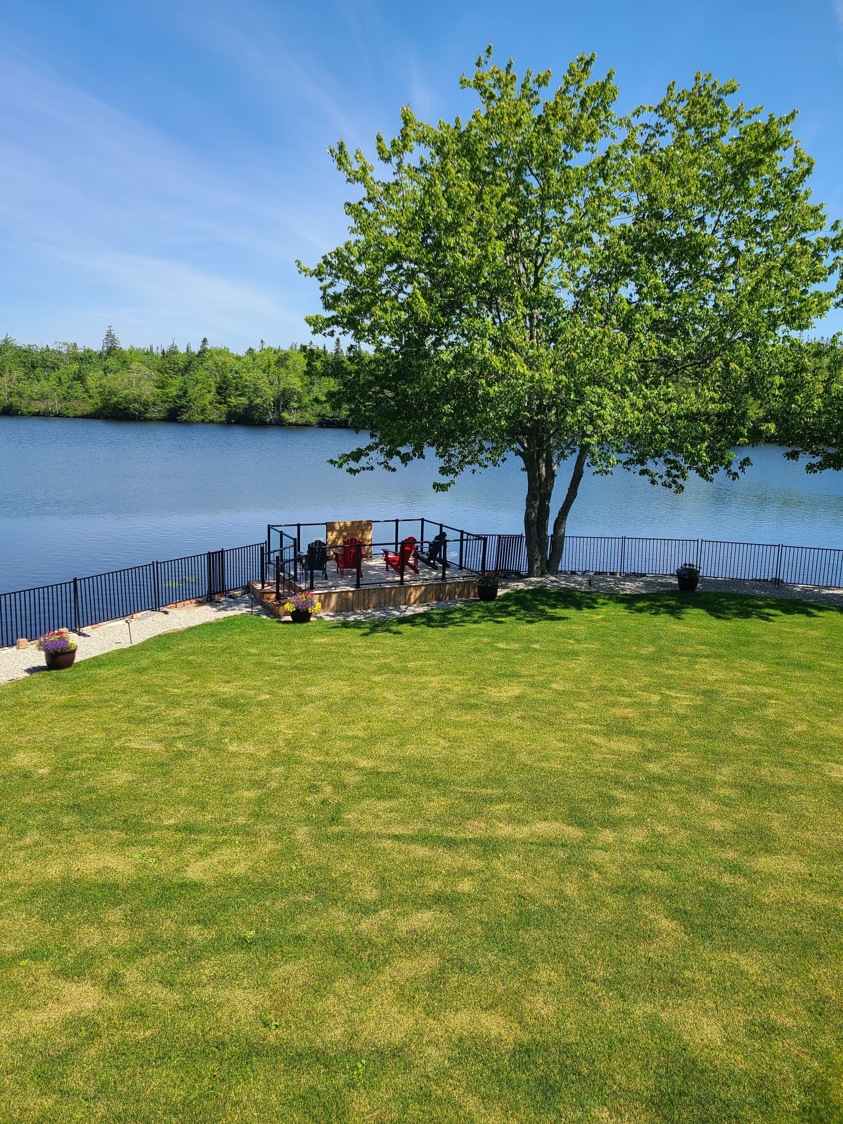 A lakeside deck with a view of the lake, surrounded by a metal railing and a grassy lawn.
