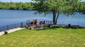 A lakeside deck with a view of the lake, surrounded by a metal railing and a grassy lawn.