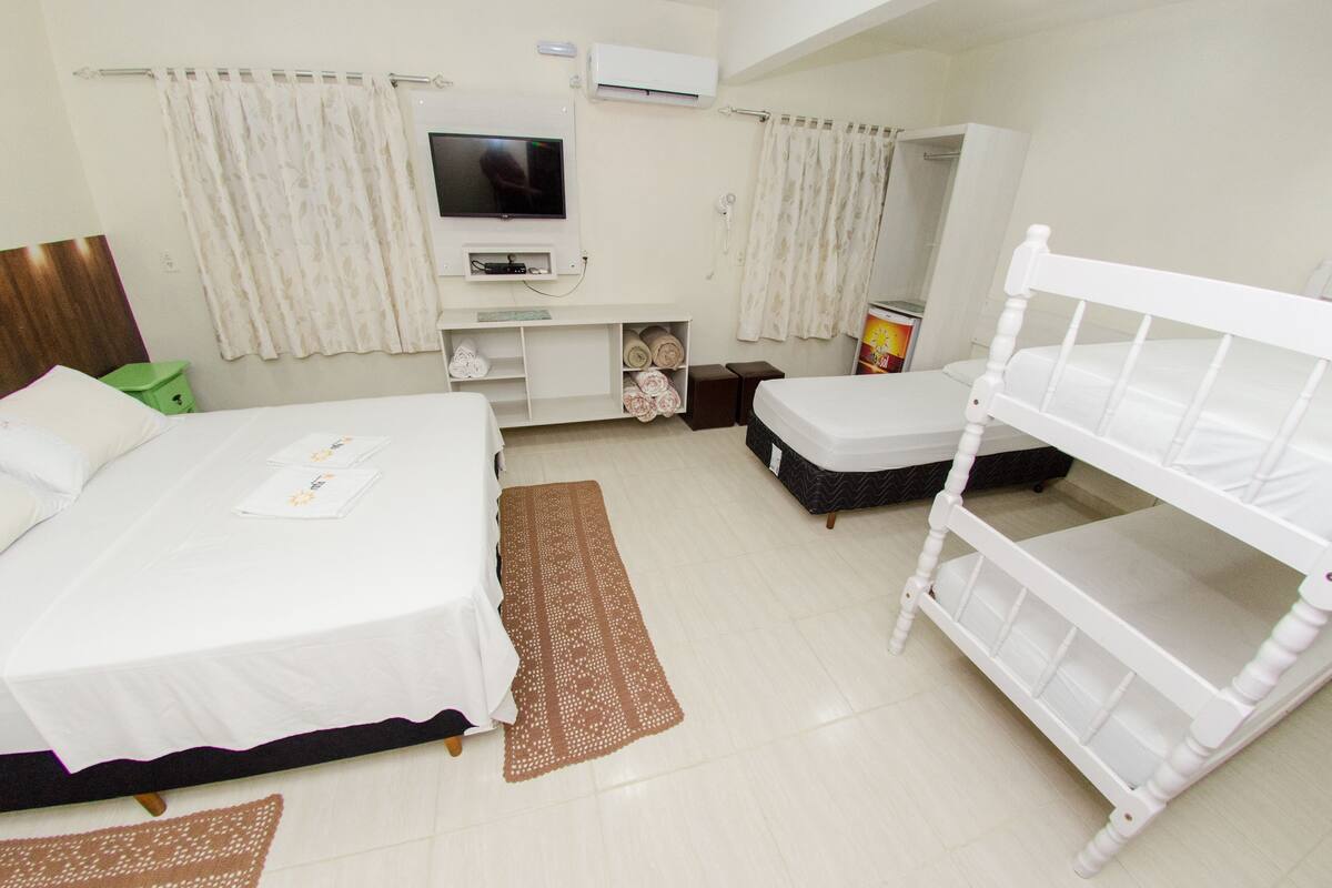 Quarto de hotel com cama, televisão, mesa pequena e um banco.