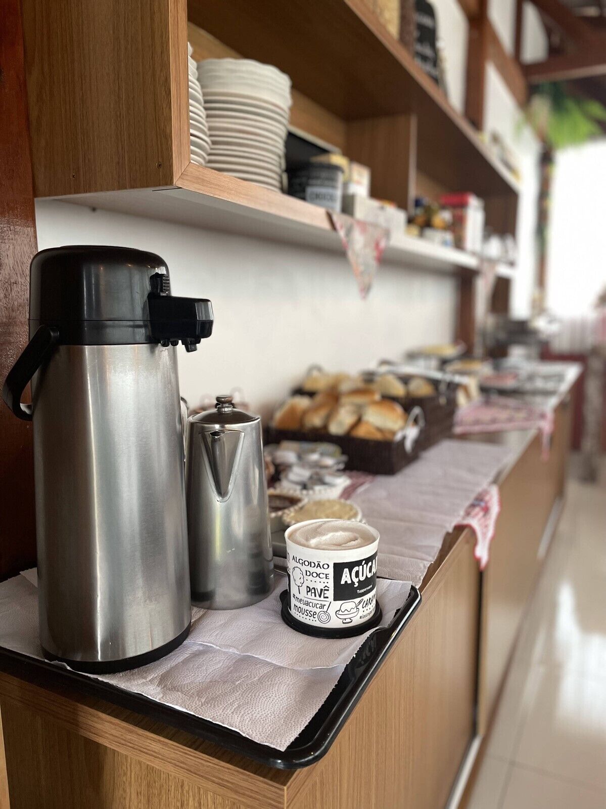 A stainless steel coffee maker and a thermos on a counter with a paper towel underneath. A jar of mousse is also visible.