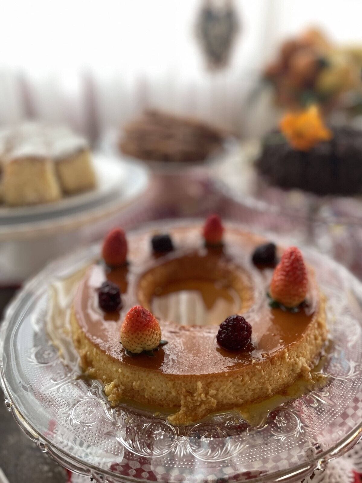 Une assiette à dessert avec un gâteau garni de fraises et de baies, et une assiette en verre ornée d’un motif décoratif.