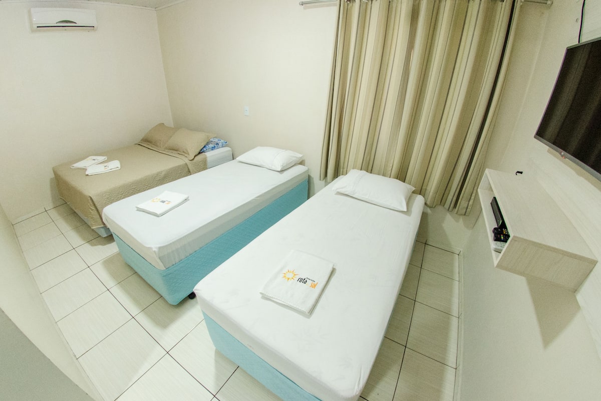 Quarto de hotel com duas camas de solteiro, televisão e uma pequena prateleira.