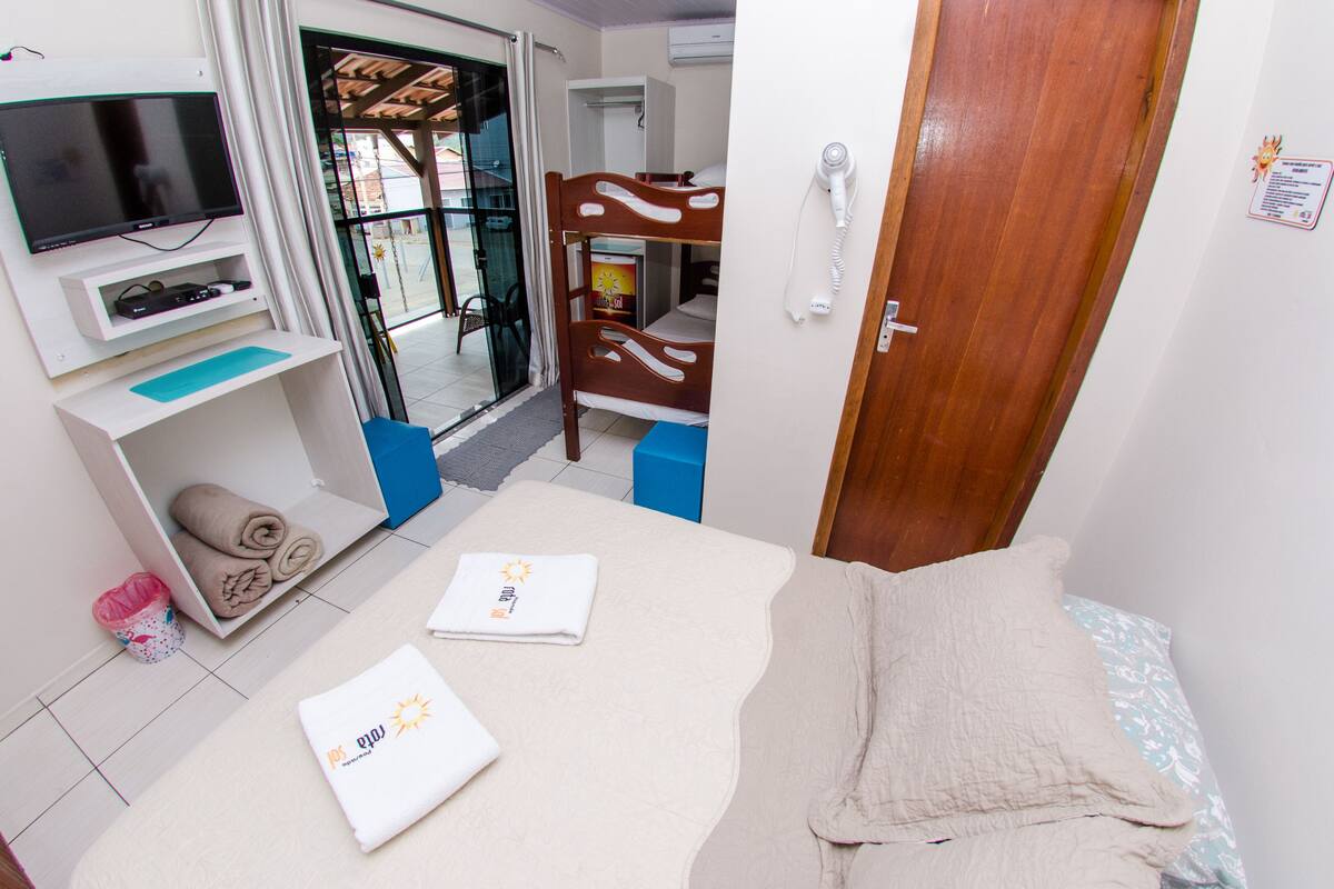 Quarto com uma cama, televisão, beliche de madeira, secador de cabelo e uma pequena lixeira.