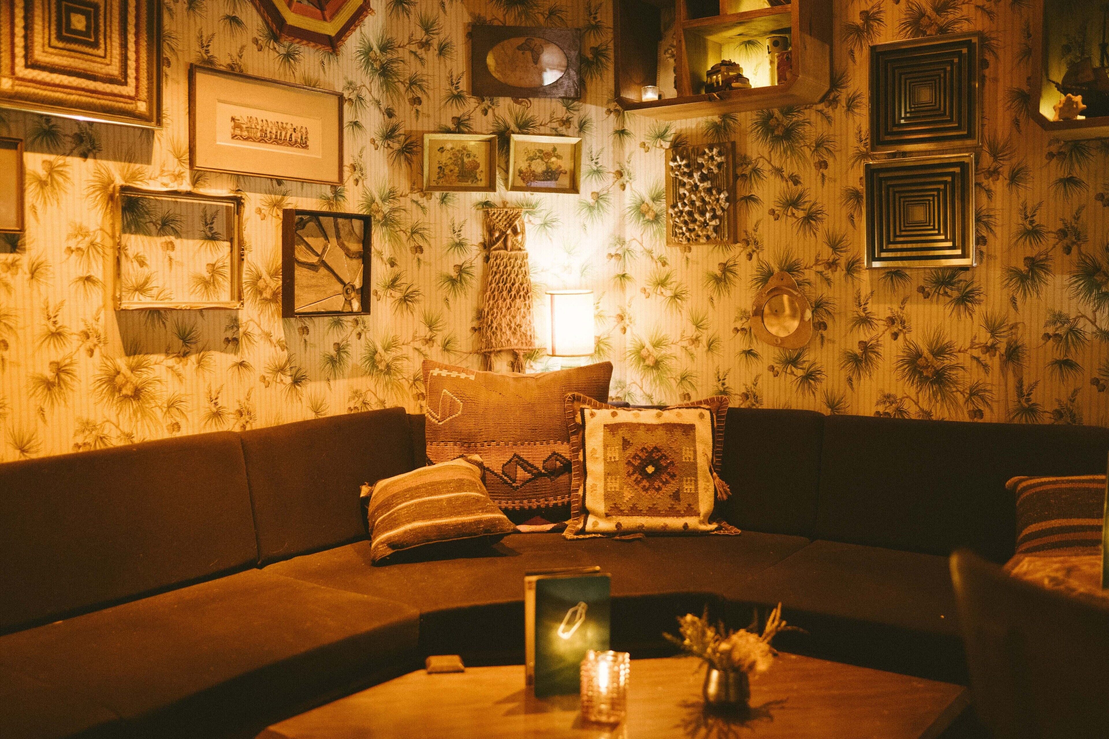 A cozy living room with a brown sofa, decorative pillows, framed artwork, and a small table with a candle and a card.