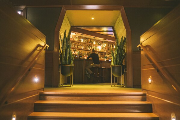 A bar area with a staircase leading up to it, surrounded by potted plants.