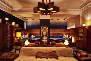 A luxurious hotel lobby with a plush sofa set, a large wooden bookshelf, and a central decorative pillar.