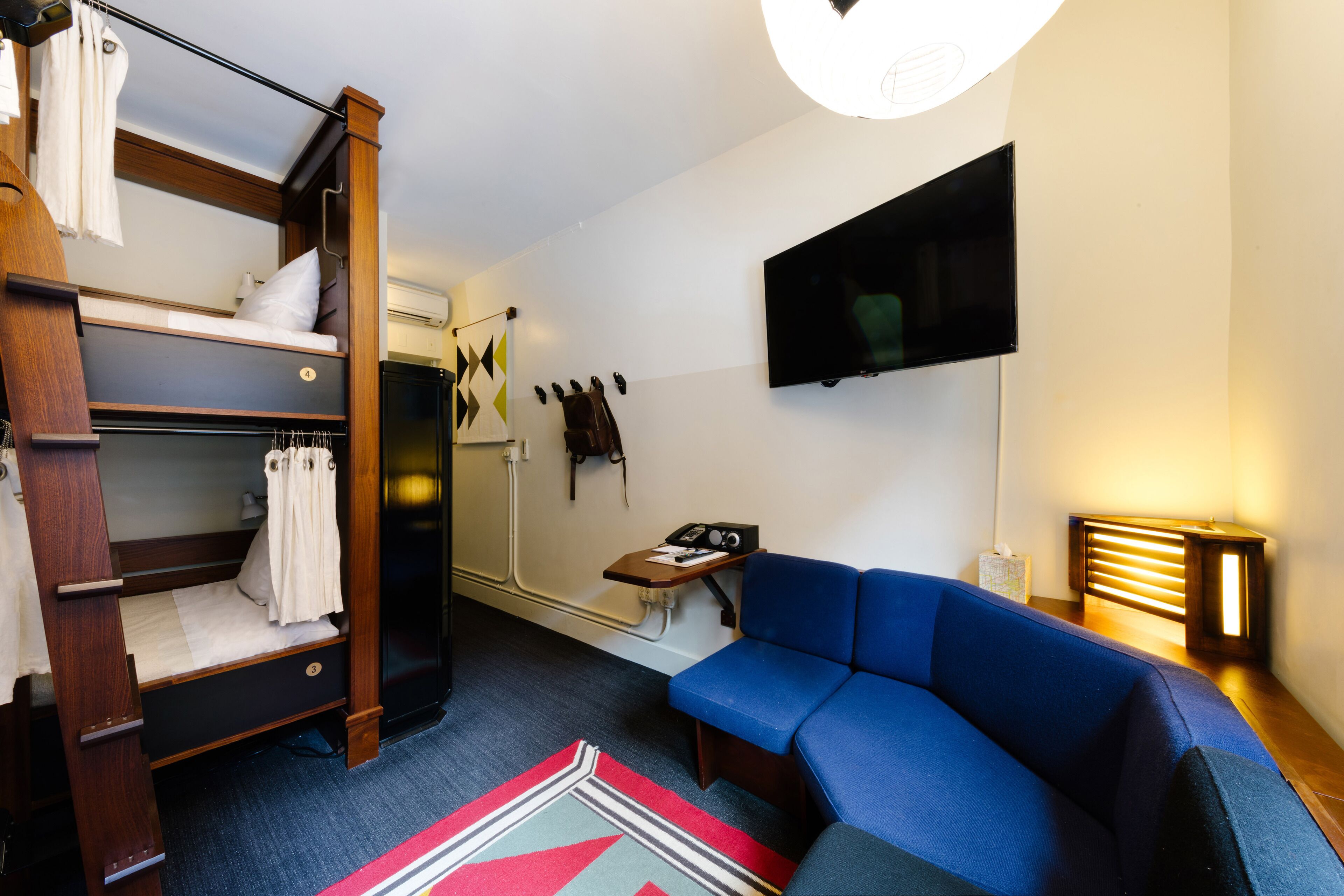 Habitación compacta con literas, un sofá azul, un televisor de pantalla plana y una pequeña mesa con lámpara.