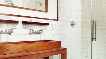 A modern bathroom with a wooden vanity, white tiled walls, a glass shower enclosure, and neatly folded towels on a shelf.