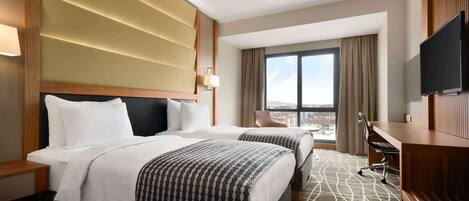 A hotel room with two beds, a desk, a chair, a TV, and a large window with a city view.