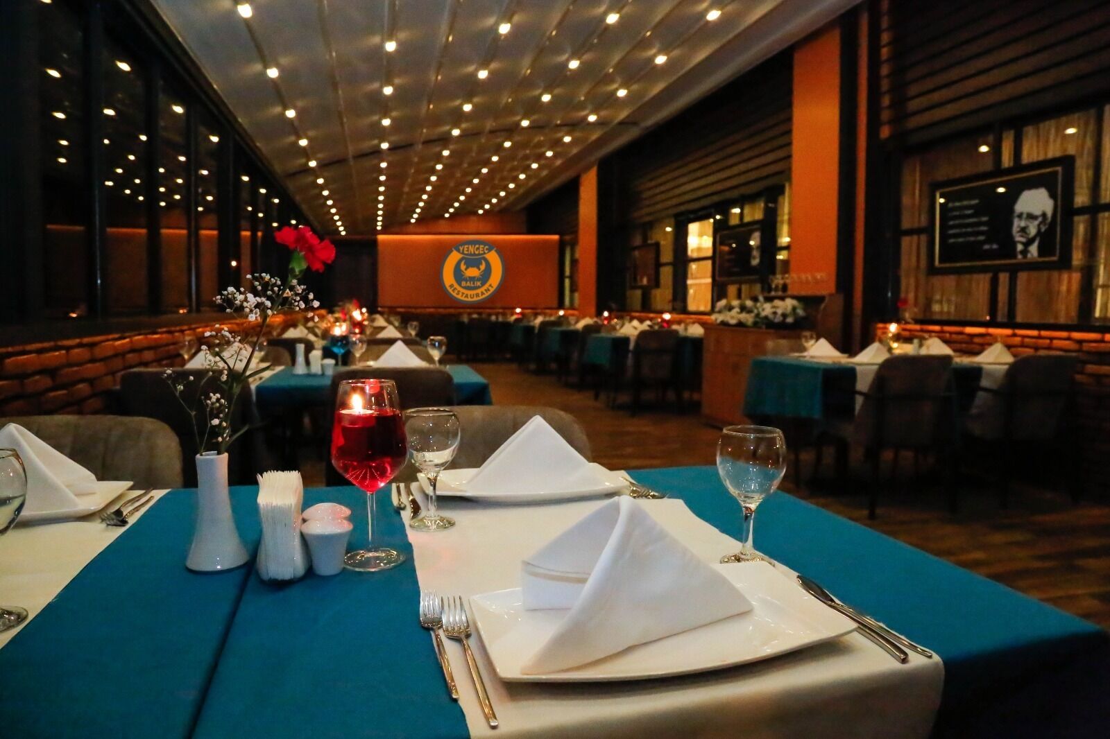 A restaurant with tables set for dining, featuring a blue tablecloth, white napkins, and wine glasses.