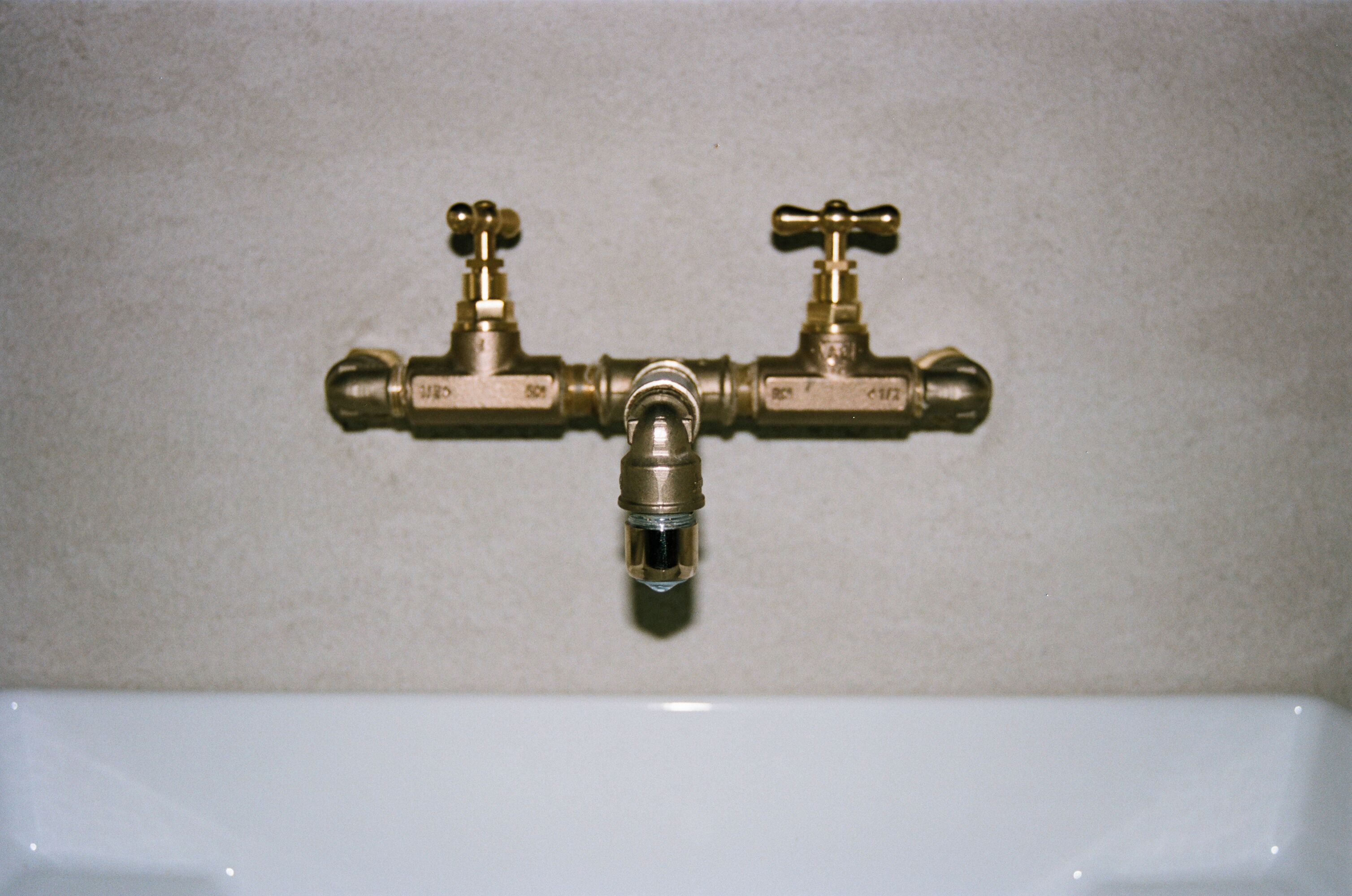 A bathroom with a white sink and two brass faucets mounted on the wall.