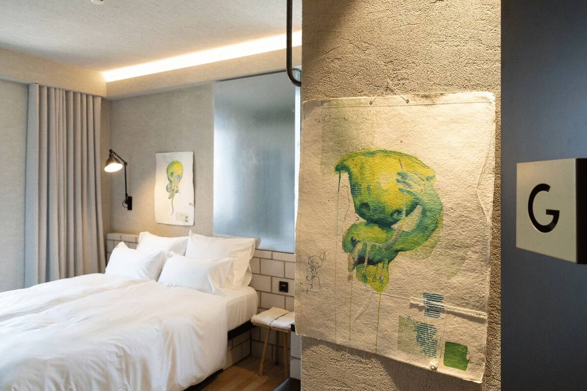 Een hotelkamer met een bed, nachtkastje, lamp en een schilderij aan de muur.