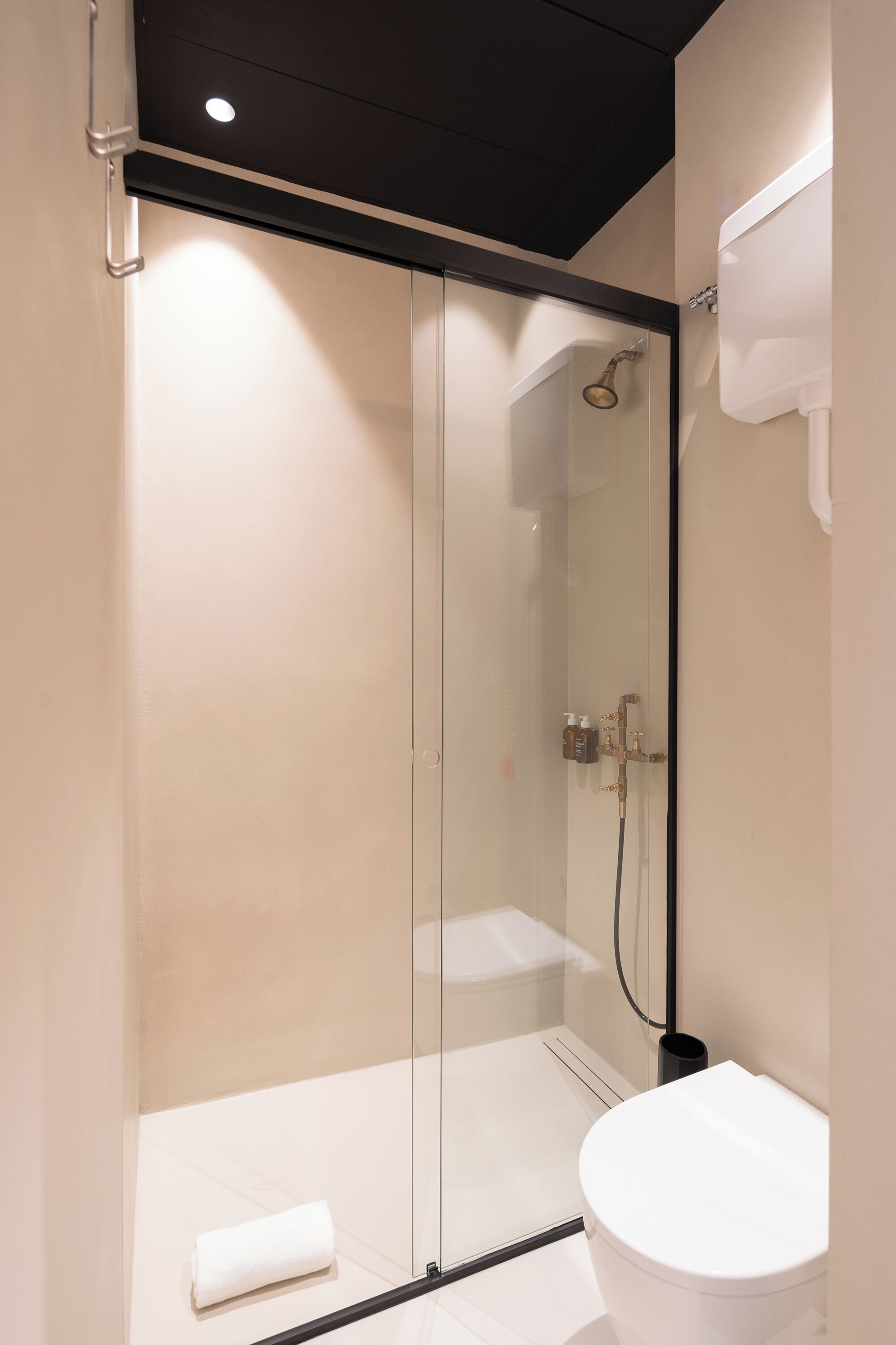 Une salle de bain moderne avec une douche à parois de verre, des toilettes blanches et une serviette sur le sol.