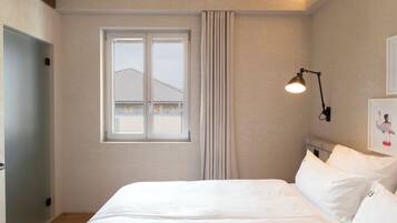 Een slaapkamer met een bed, een raam, een gordijn, een wandlamp en een deur.
