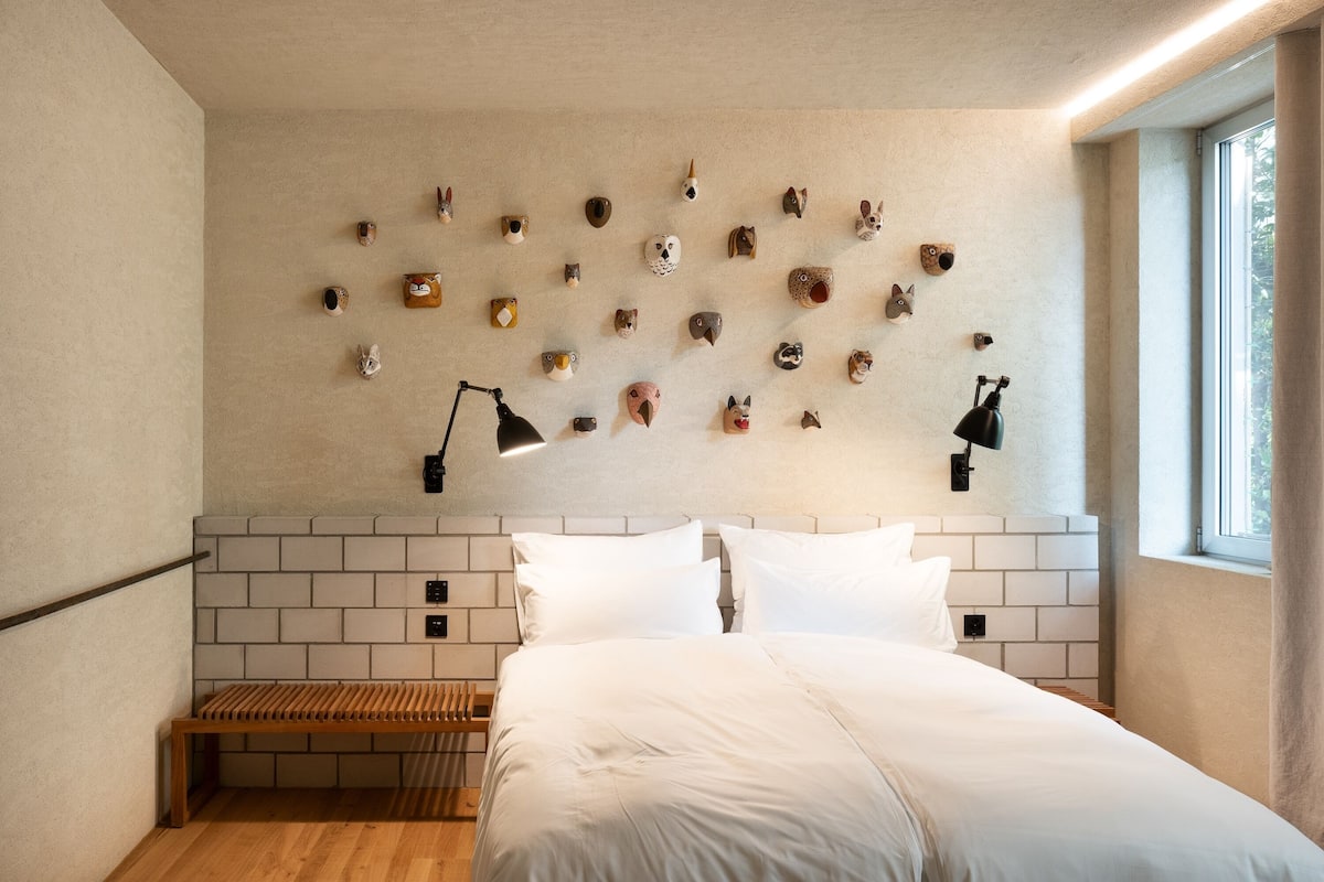 Een moderne slaapkamer met een hoofdeinde met een bakstenen patroon, een houten bankje en een muur versierd met diverse beeldhouwwerken van dierenkoppen.