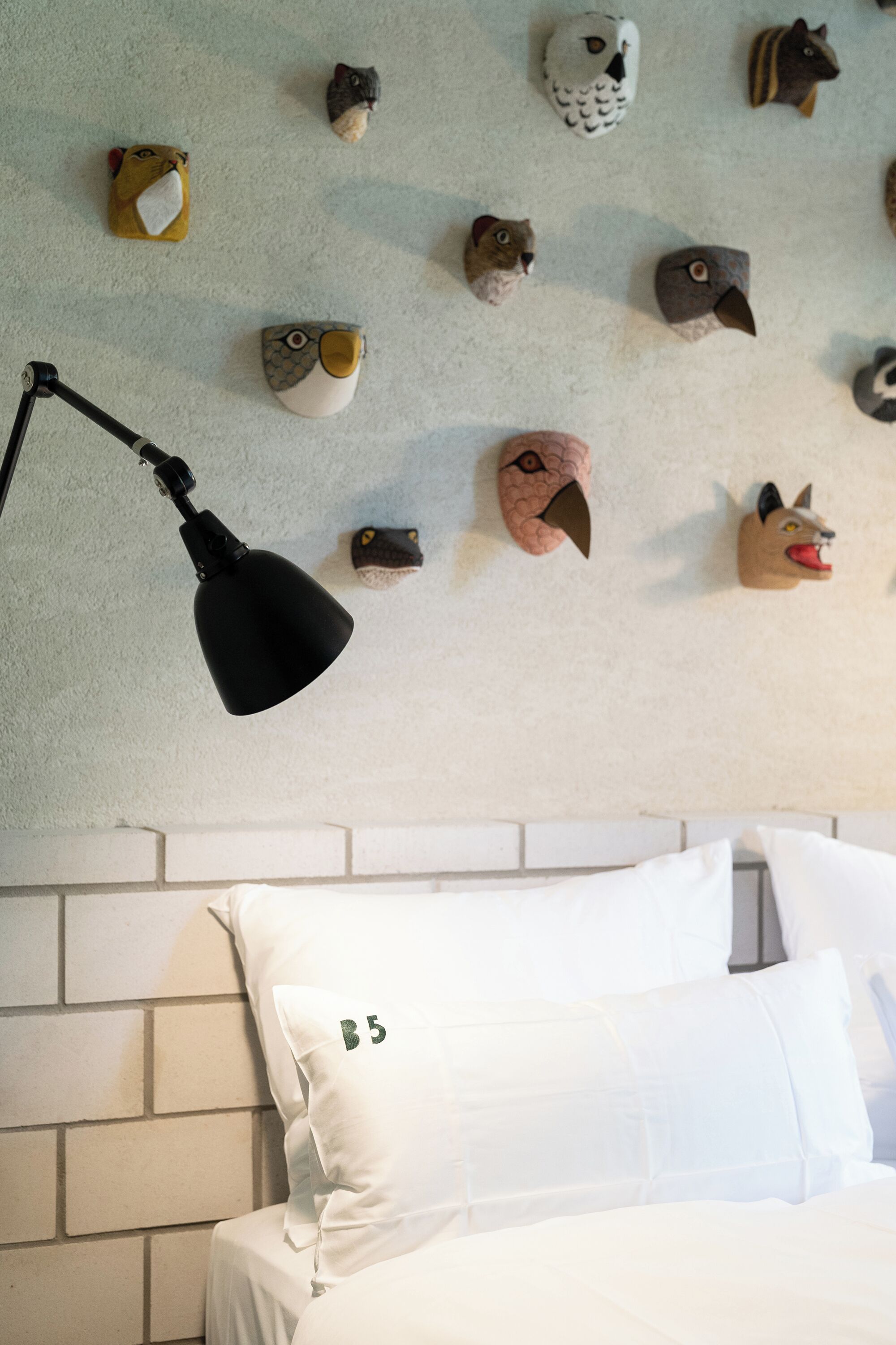 A bed with white bedding and pillows, a black lamp, and a wall decorated with various animal head sculptures.