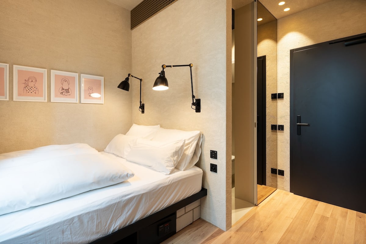 Een moderne slaapkamer met een bed, nachtlampjes en een lijst met kunst aan de muur.