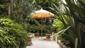 Un patio jardín con una sombrilla central, asientos de madera y abundante vegetación.