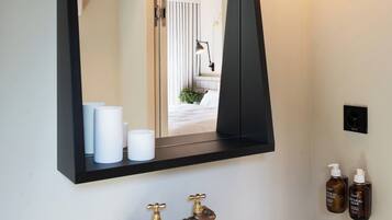Une salle de bain avec un lavabo blanc, un miroir noir et un luminaire fixé au mur.
