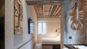 Un dormitorio con techo de madera, una cama, un ventanal y una lámpara fijada a la pared.