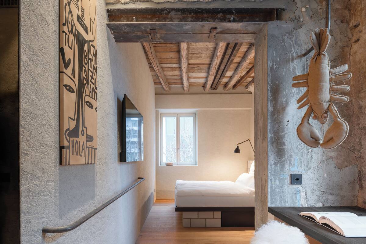 Een slaapkamer met een houten plafond, een bed, een raam en een wandlamp.