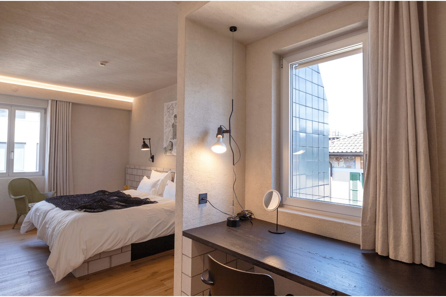 Et soveværelse med seng, sengebord, lampe og et vindue med gardiner.