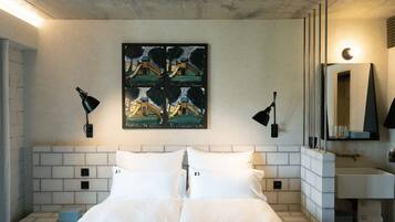 Hotelkamer met een bed, een betegeld hoofdeinde, een schilderij van een speeltuin, twee wandlampen, een spiegel en een klein nachtkastje.