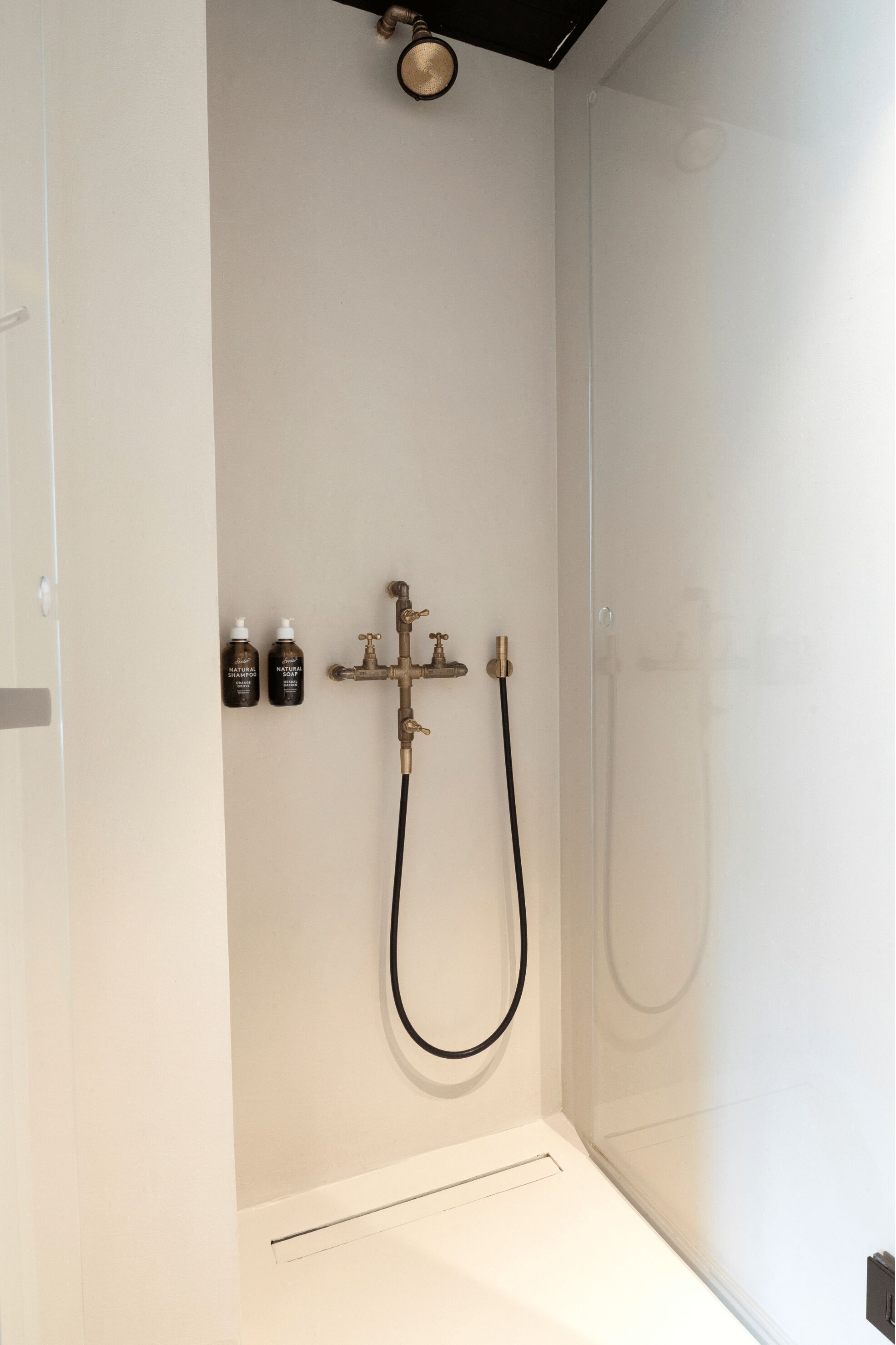 Ducha con cabezal de ducha de mano, grifo empotrado en la pared, dos botellas de champú y un extractor.