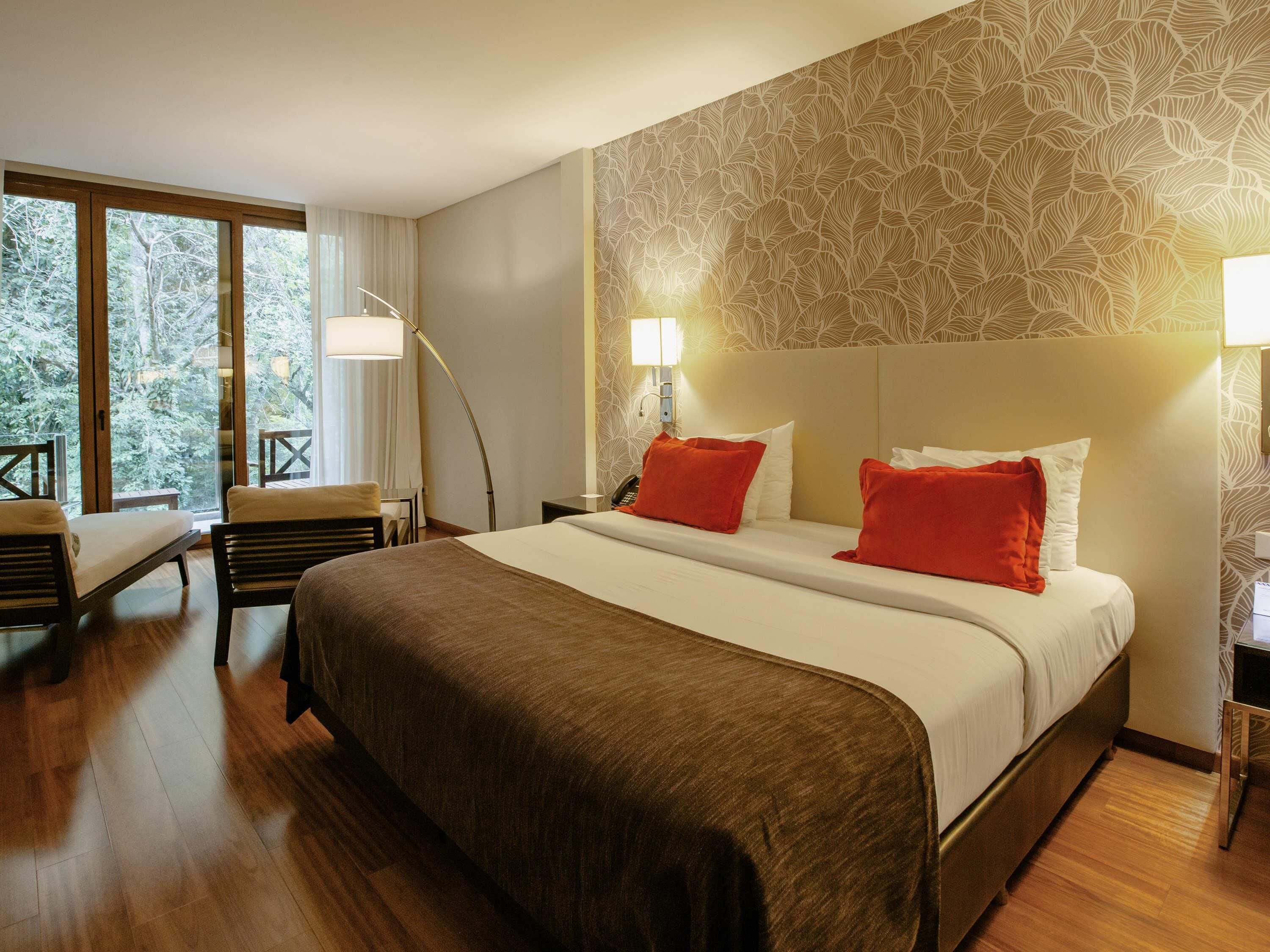 A hotel room with a large bed, two bedside tables, a desk with a chair, and a window with curtains.