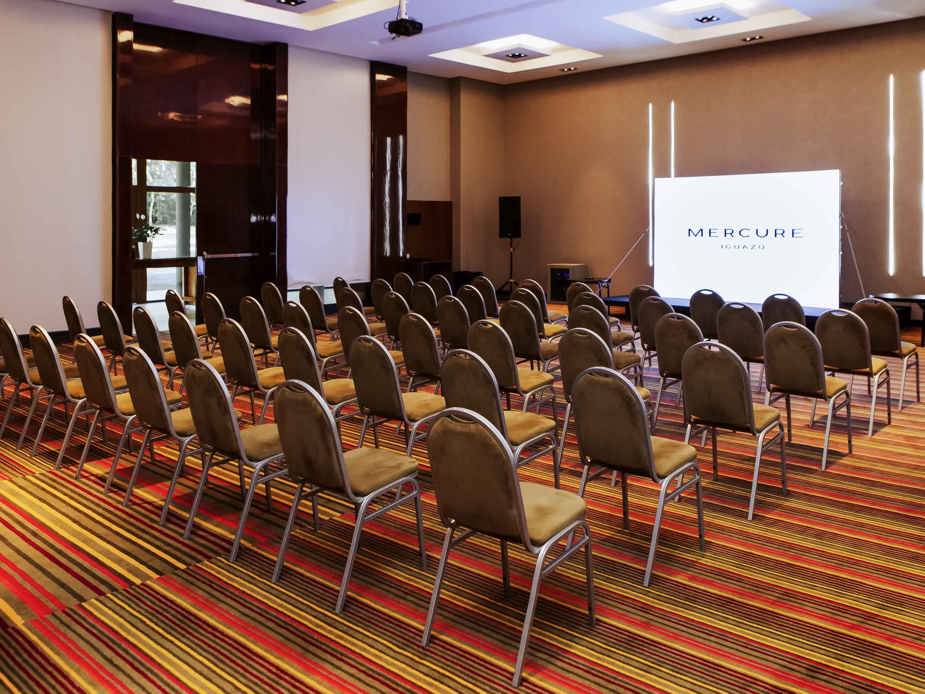 A conference room with rows of chairs, a projection screen, and a carpeted floor.