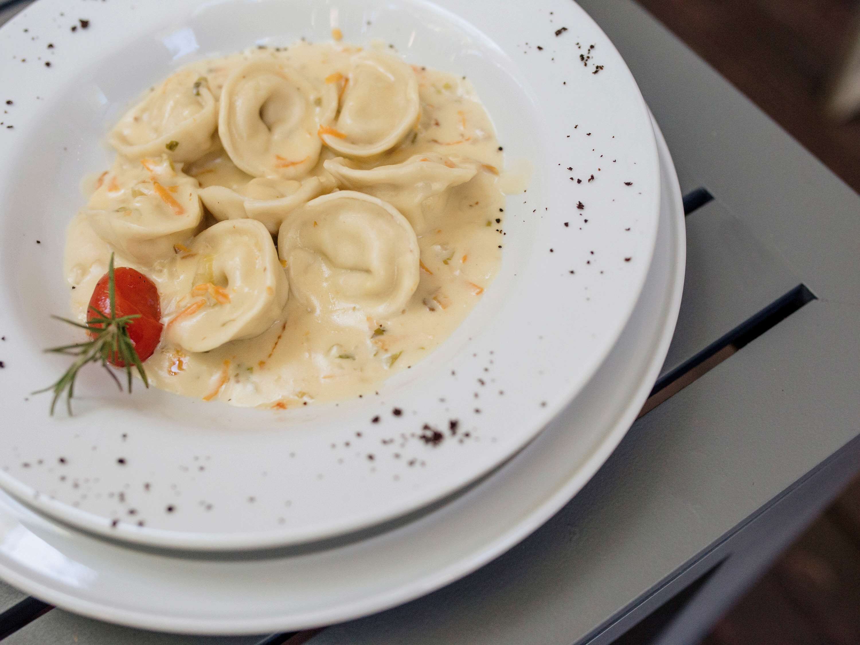 A plate of ravioli in a creamy sauce with a garnish of rosemary and a cherry tomato.