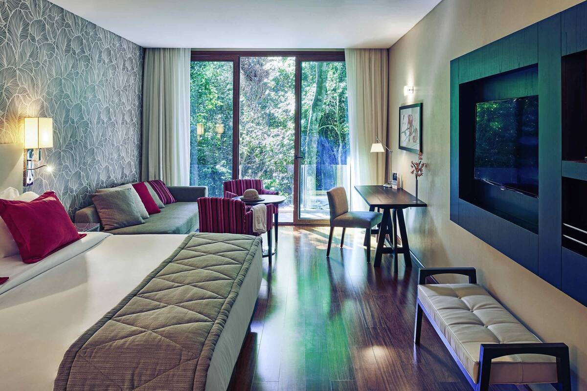 A hotel room with a bed, a sofa, a dining table, and a TV.