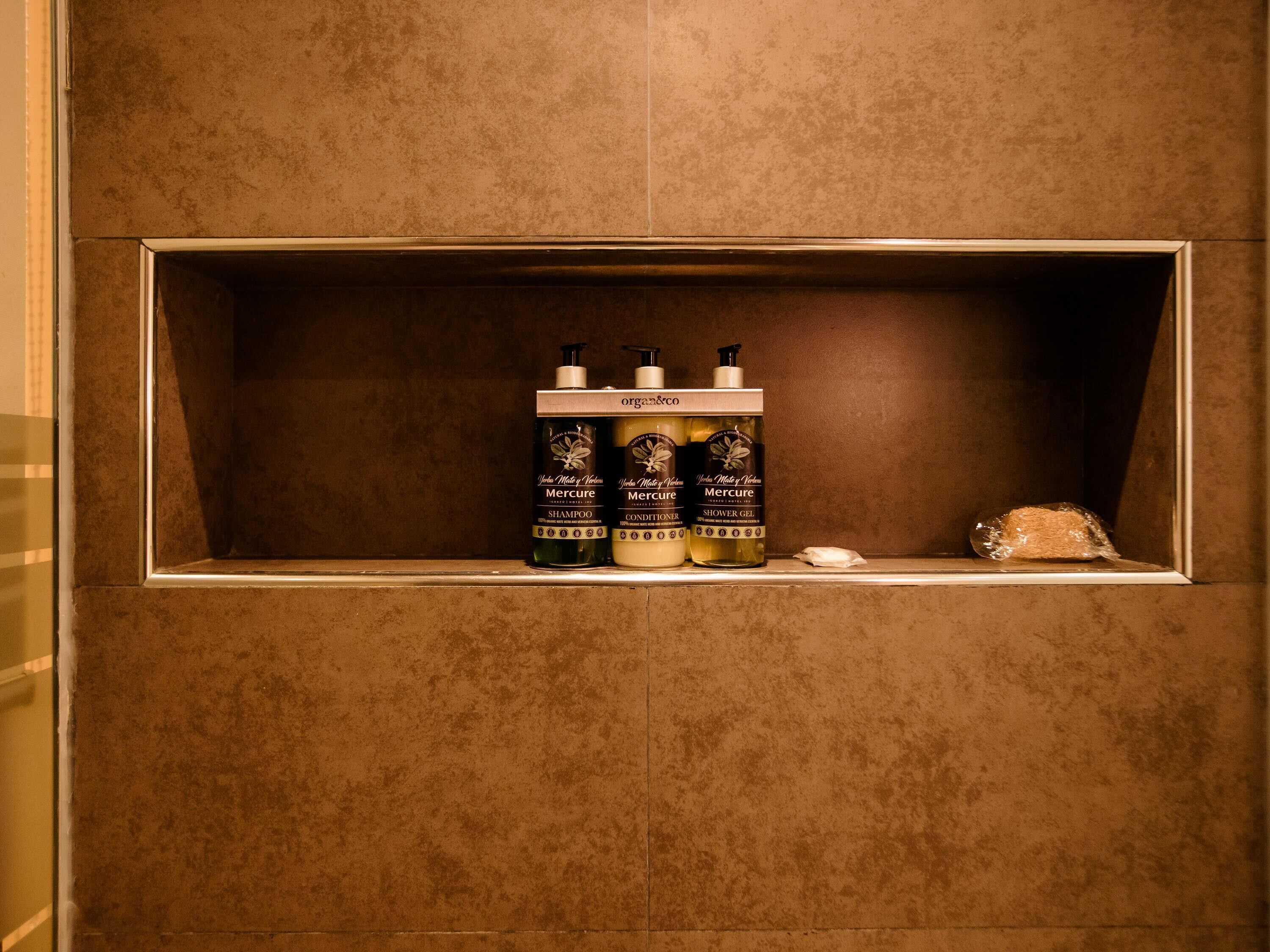 A bathroom shelf with three bottles of shampoo, conditioner, and shower gel.