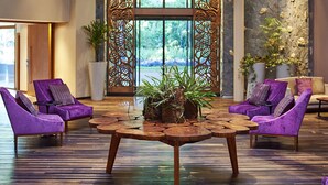 Un vestíbulo con una mesa redonda de madera, sillas moradas y una puerta metálica decorativa.