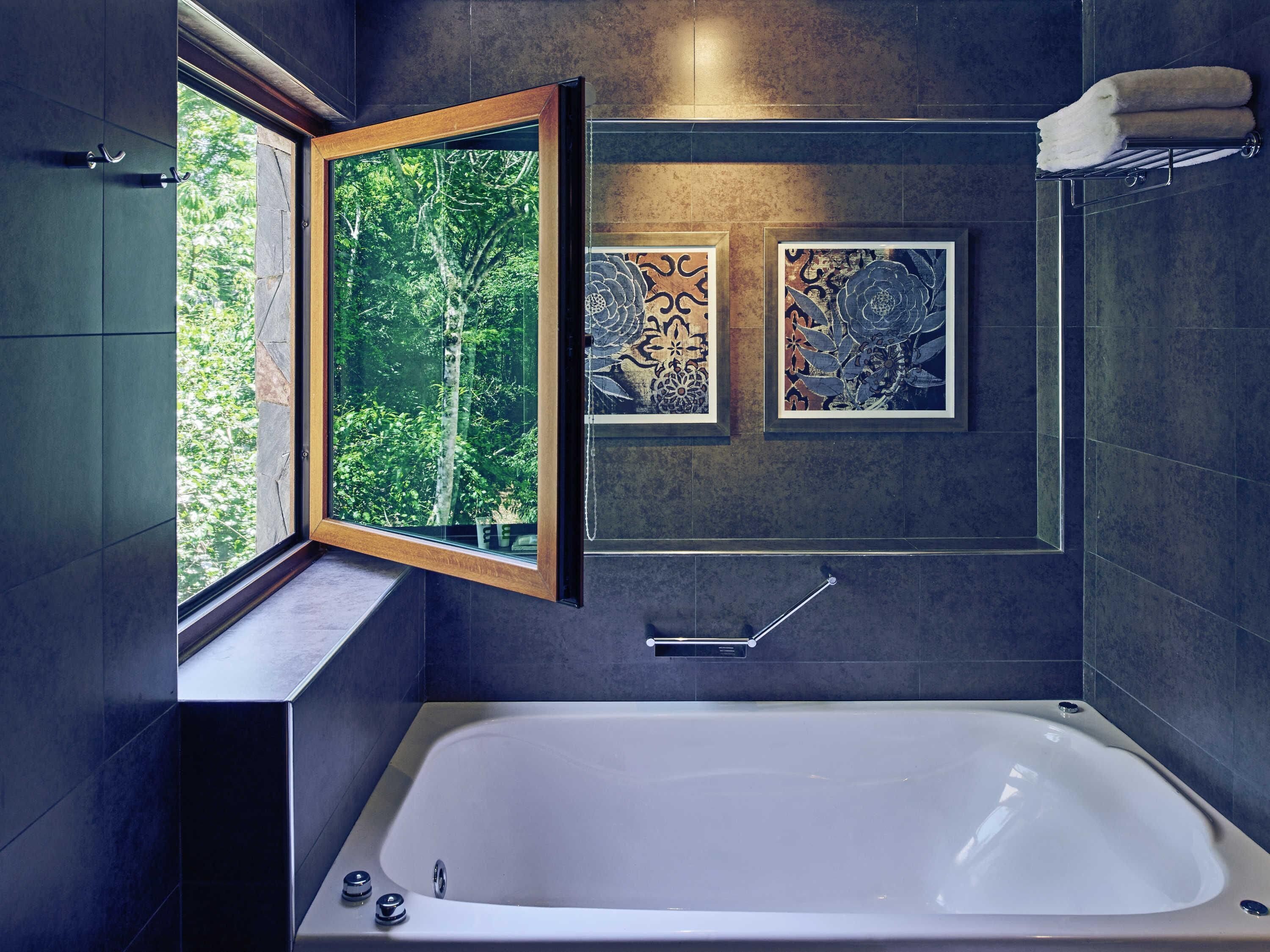 A modern bathroom with a bathtub, a window with an open frame, and two framed wall art pieces.