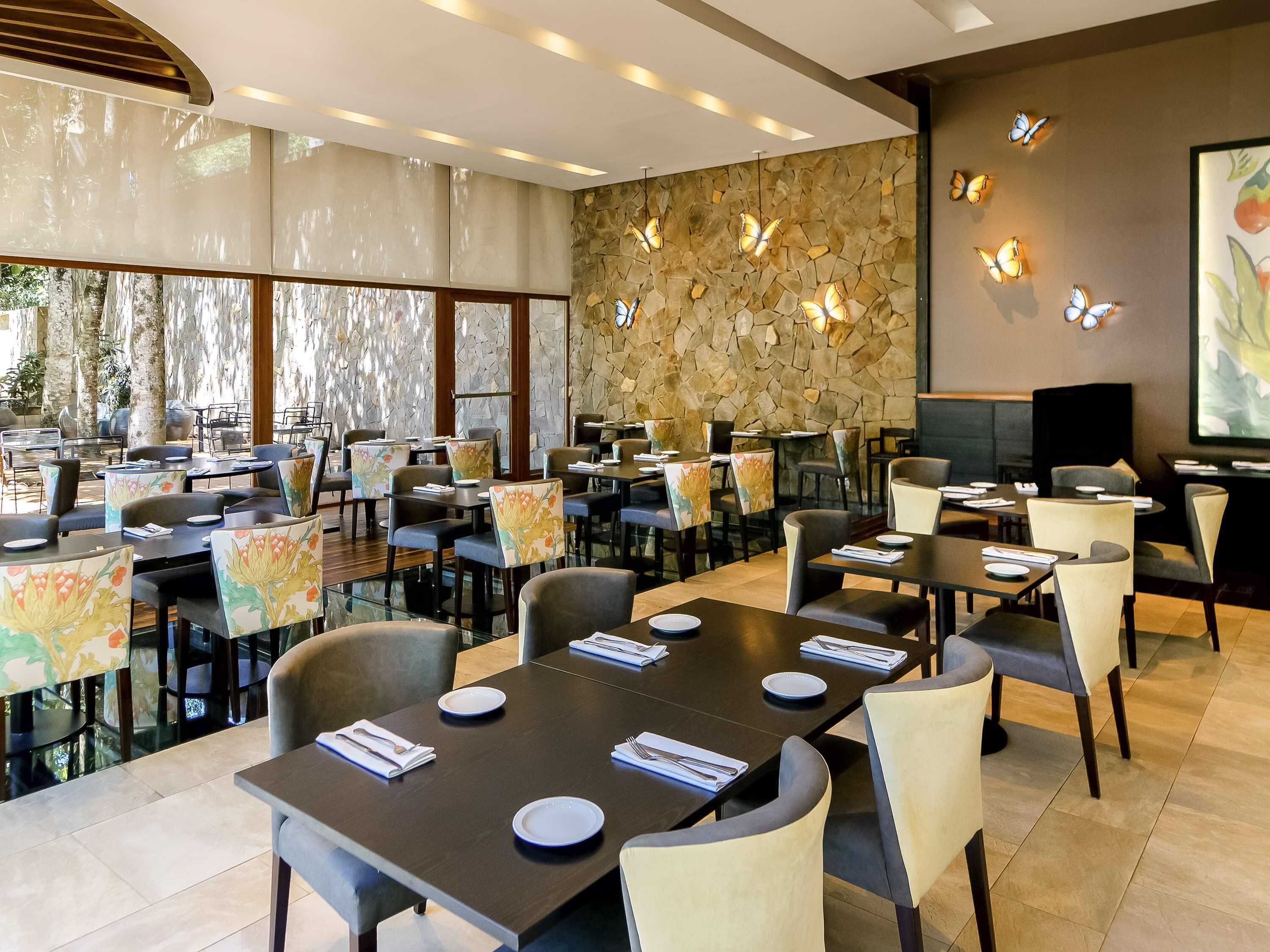A restaurant with tables set for dining, a stone wall, and butterfly wall sconces.