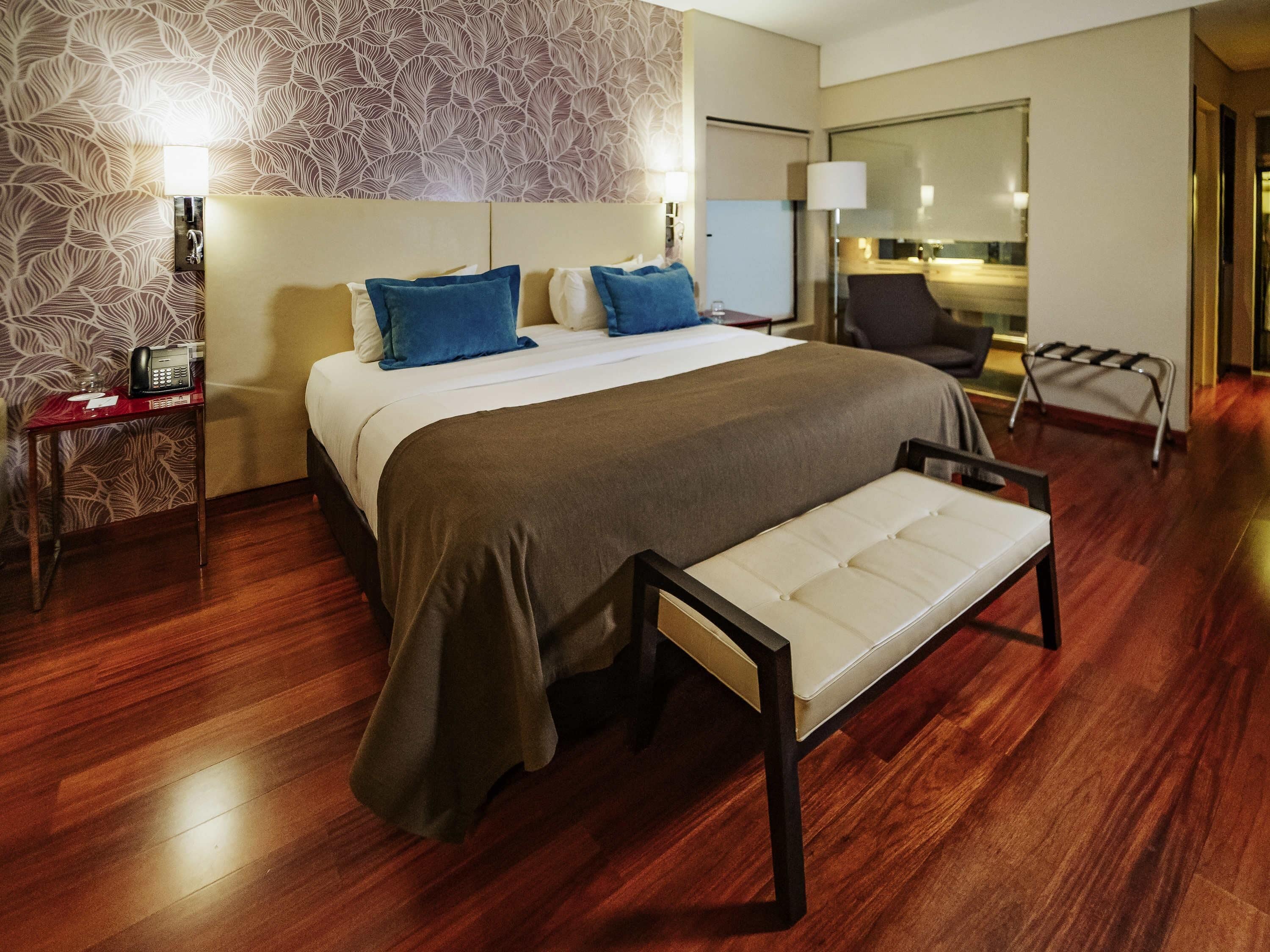 A hotel room with a bed, bedside table, lamp, and a view of the room's interior.