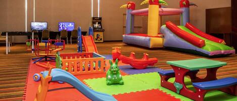 Un área de juegos interior con tobogán, piscina de pelotas y estructuras hinchables.