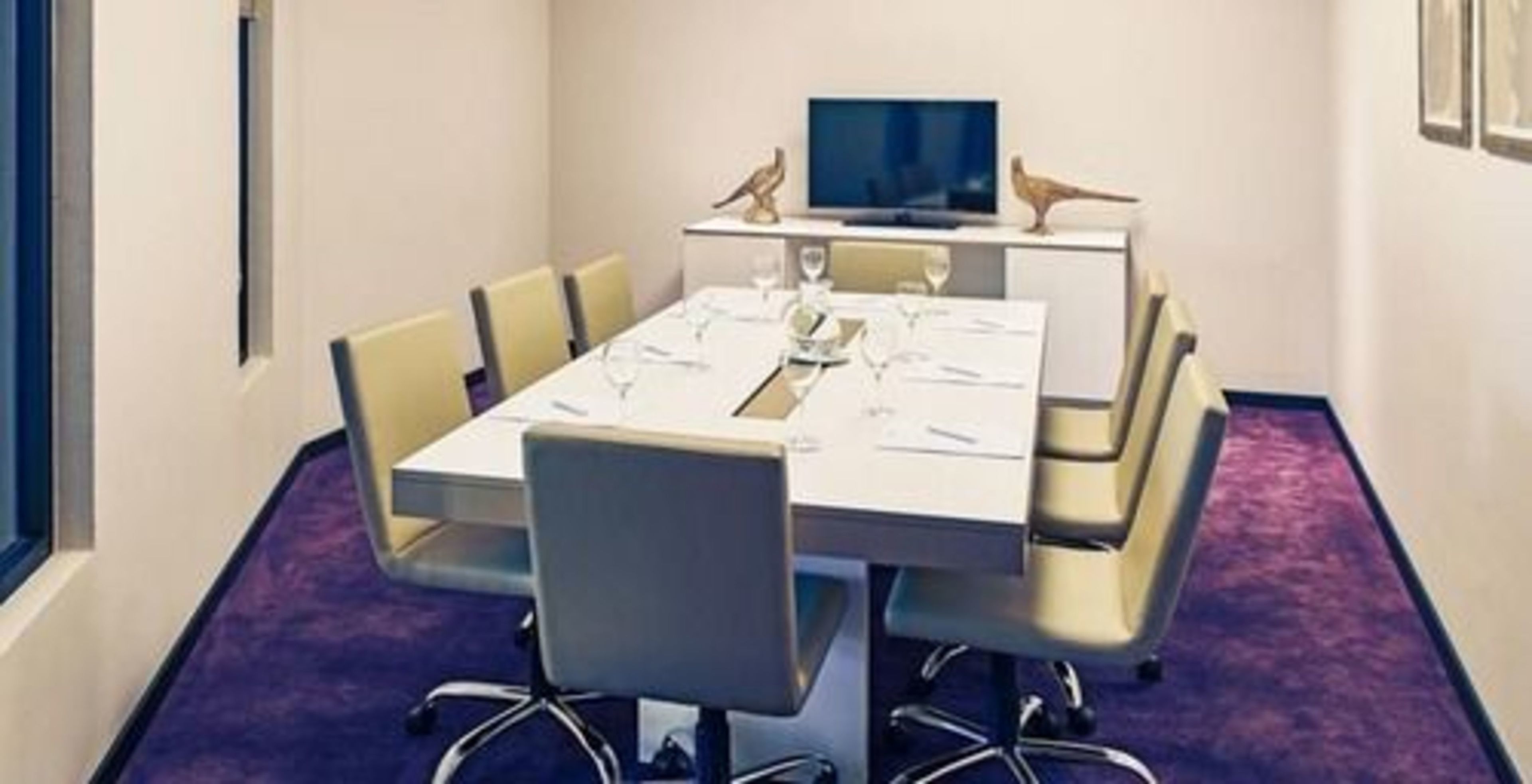 Ein Konferenzraum mit einem weißen Tisch, vier Stühlen, einem Fernseher und einem kleinen dekorativen Vogel auf dem Tisch.