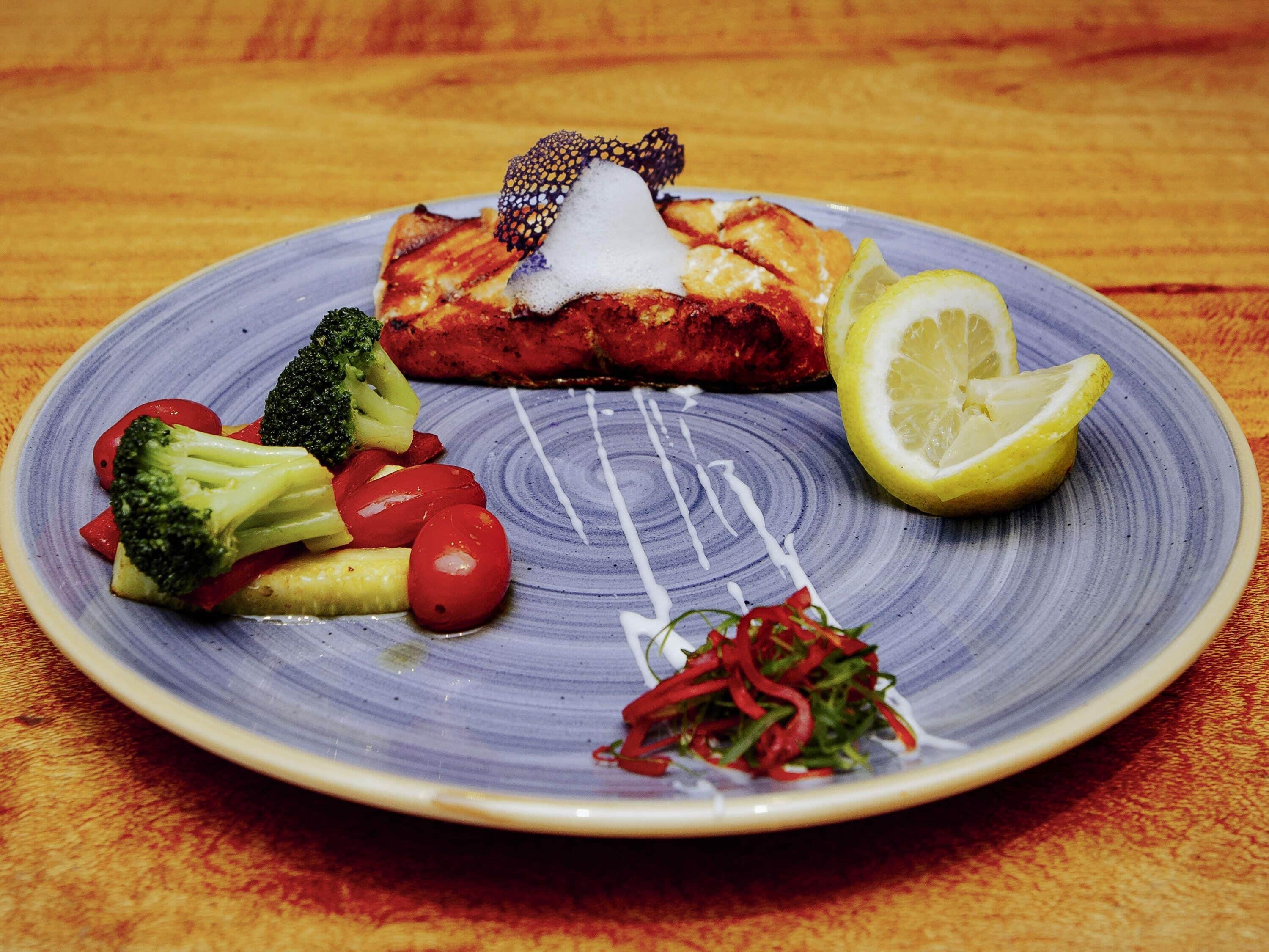 A plate with grilled fish, broccoli, cherry tomatoes, lemon, and a side salad.