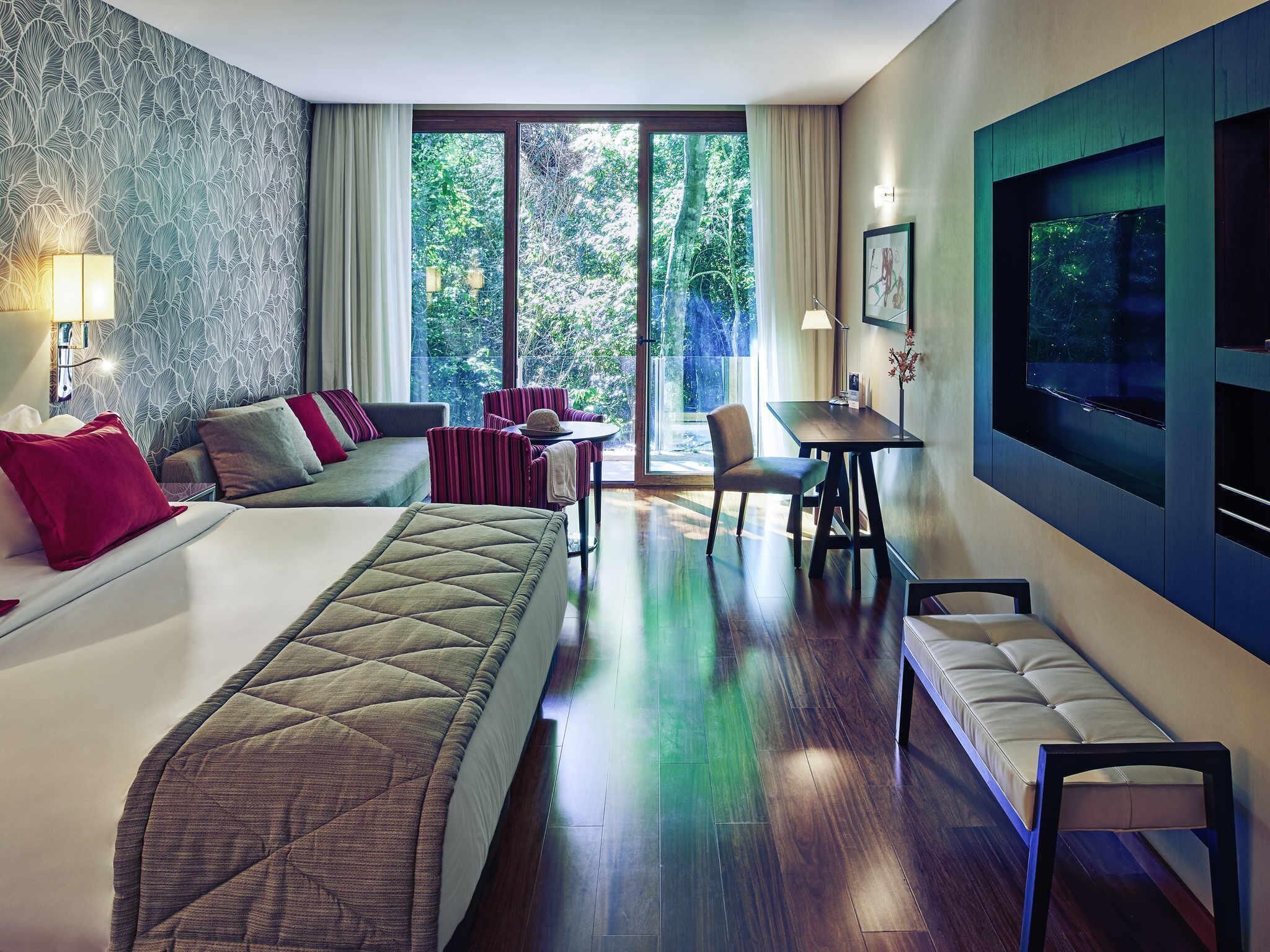 Quarto de hotel com uma cama grande, um sofá, uma mesa de jantar e uma televisão.