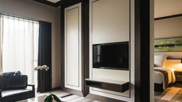 A modern hotel room with a flat-screen TV mounted on a wall, a sofa, a coffee table, and a painting on the wall.